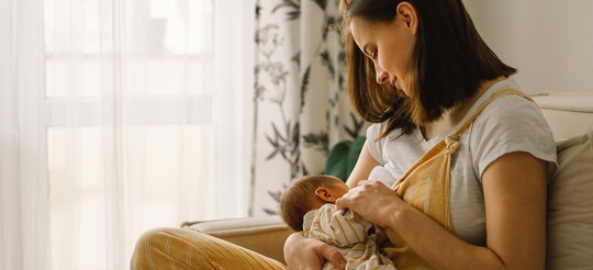 Frau mit Halsschmerzen stillt ihr Baby: In der Stillzeit empfiehlt es sich, ärztlich abzusprechen, welche Medikamente geeignet sind.