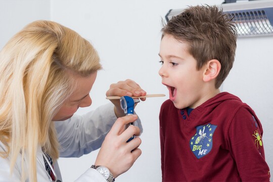 Fürsorgliche Unterstützung bei Halsschmerzen im Kindesalter – draußen auf dem Spielplatz Frau spricht mit einem traurigen Kind auf dem Spielplatz; das Kind hält sich den Hals, möglicherweise wegen Halsschmerzen.